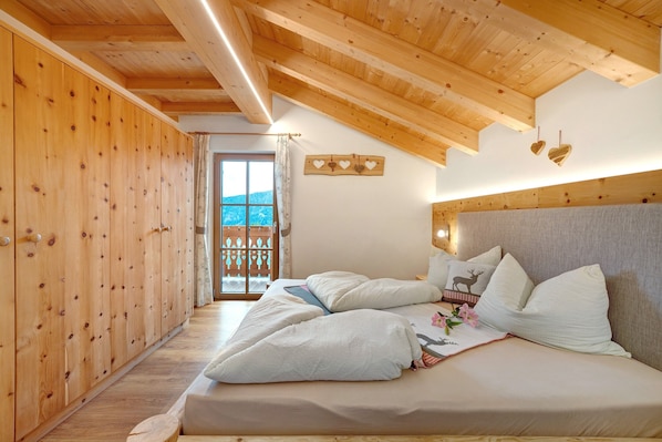 Ein Schlafzimmer mit Holzwänden, einem Bett mit weißer Bettwäsche und Blick ins Freie.