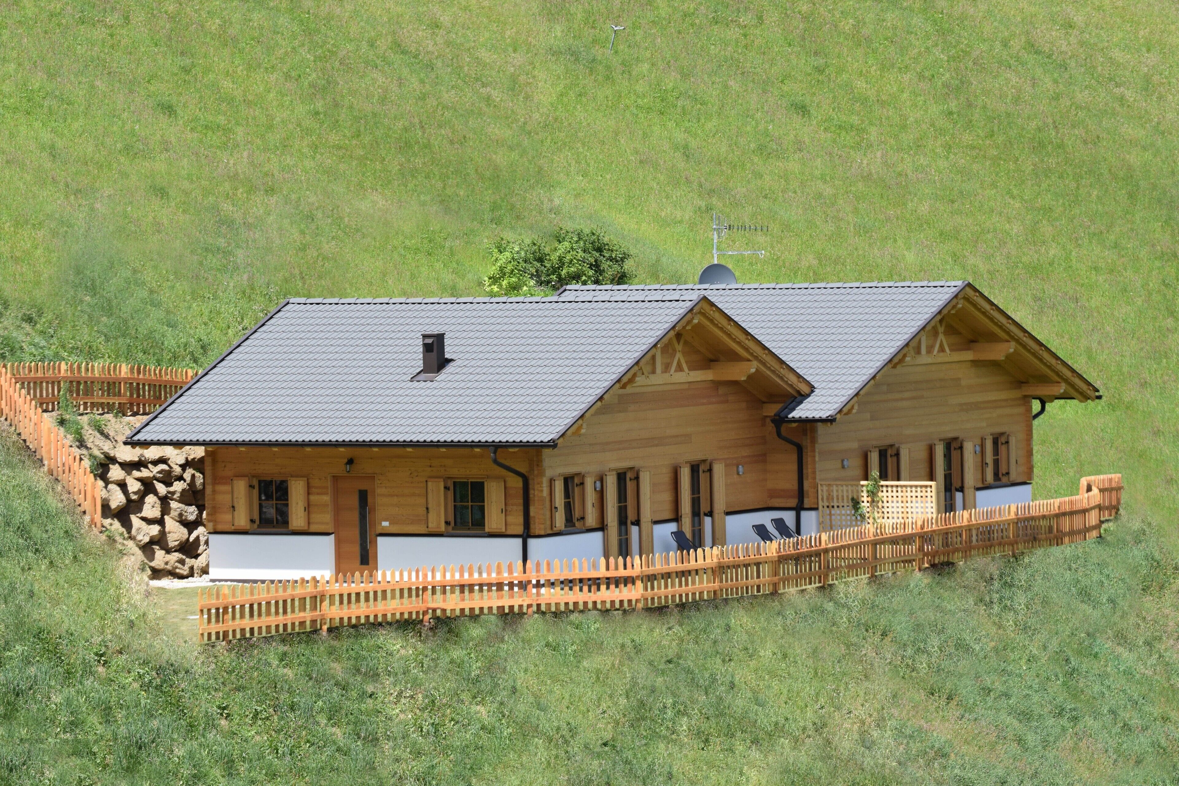 Eine Holzhütte mit geneigtem Dach, einem Steinfundament und einem Holzzaun darum herum.