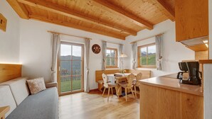 A cozy room with a wooden ceiling, a sofa, a dining table with chairs, and a kitchen area with a coffee machine. - Chalet 'Niederhaushof  Edelweiß' with Mountain View, Private Garden and Wi-Fi (Ulten)