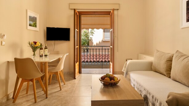 Ein Wohnzimmer mit Sofa, einem Esstisch mit Stühlen, einem an der Wand montierten Fernseher und einem Balkon mit Blick.