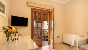 Ein Zimmer mit Esstisch, Stühlen, einem an der Wand befestigten Fernseher, einem Bett und einer Tür zum Balkon.