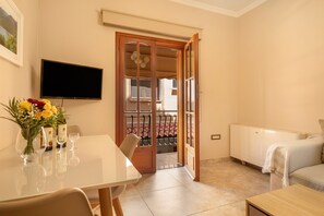 Une pièce comprenant une table à manger, des chaises, un téléviseur fixé au mur, un lit et une porte donnant sur un balcon.