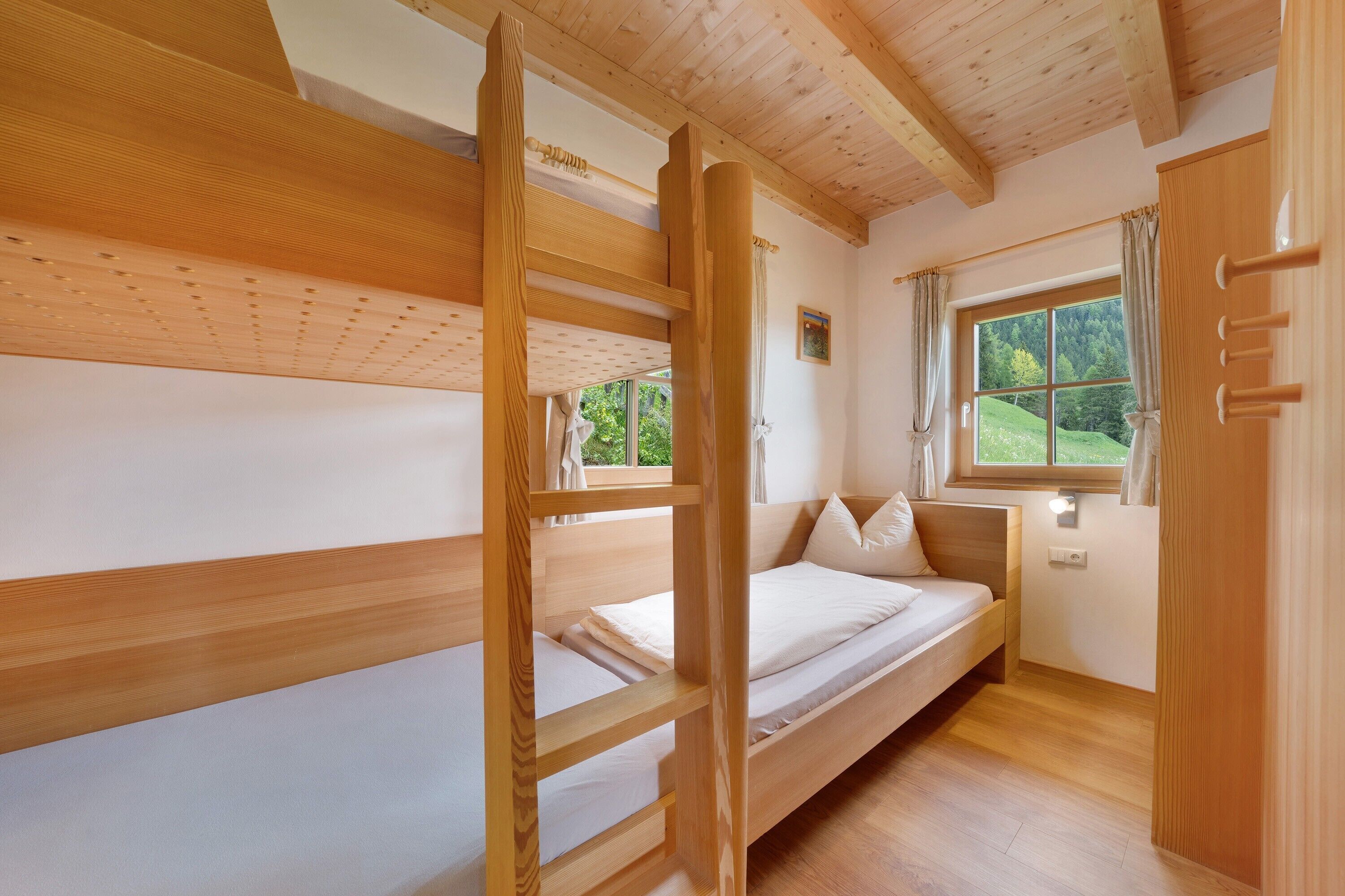 Une chambre avec un lit superposé, un plafond en bois, une fenêtre avec des rideaux et une table de chevet.