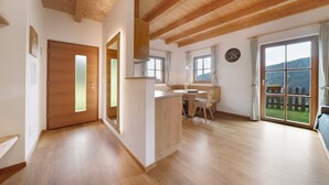 Una habitación amplia con suelo y techo de madera, un comedor con mesa y sillas, y un gran ventanal con vistas a la montaña.