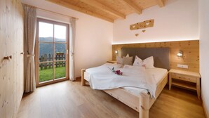 Un dormitorio de madera con una ventana grande, una cama, mesitas de noche y vistas a una valla de madera y follaje.
