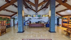 A spacious lobby with high ceilings, wooden beams, a central reception desk, and a mural on the back wall. - Tiantang Mountain Original Ecological Resort (Guangde)