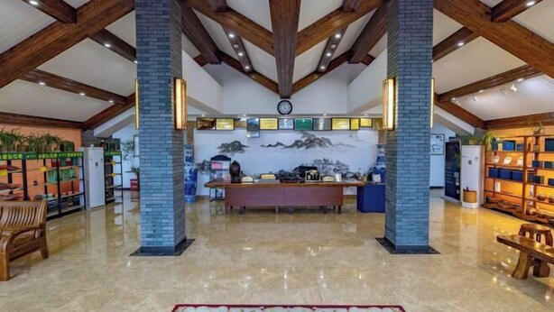 A spacious lobby with high ceilings, wooden beams, a central reception desk, and a mural on the back wall. - Tiantang Mountain Original Ecological Resort (Guangde)
