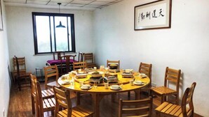 A dining area with a round table surrounded by wooden chairs, a window with blinds, and a framed calligraphy piece on the wall. - Tiantang Mountain Original Ecological Resort (Guangde)