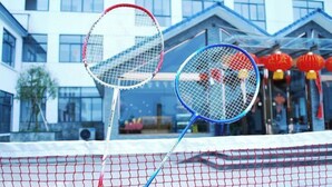 A badminton court with two rackets in the foreground and a building with large windows in the background. - Tiantang Mountain Original Ecological Resort (Guangde)