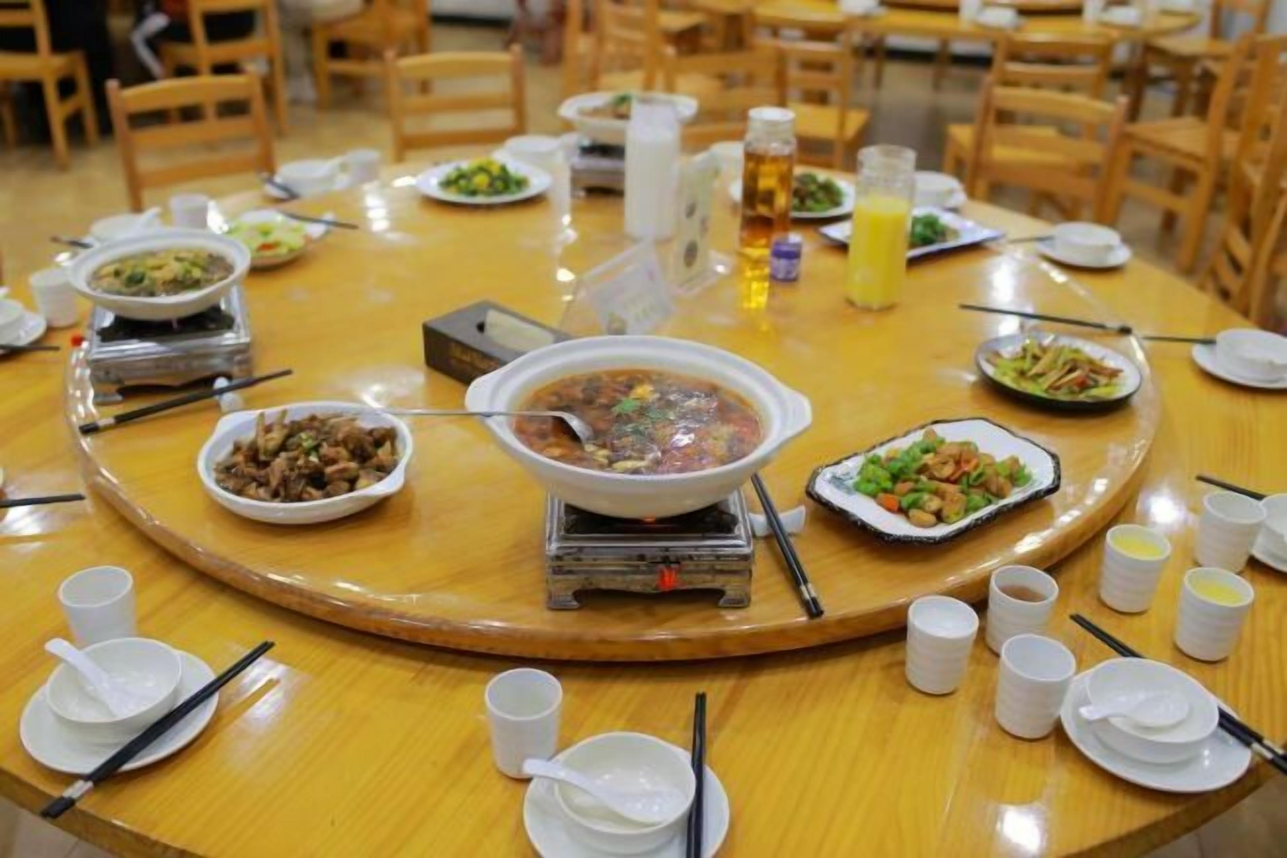 A round dining table with various dishes, including a hot pot, bowls of food, and plates of vegetables.
