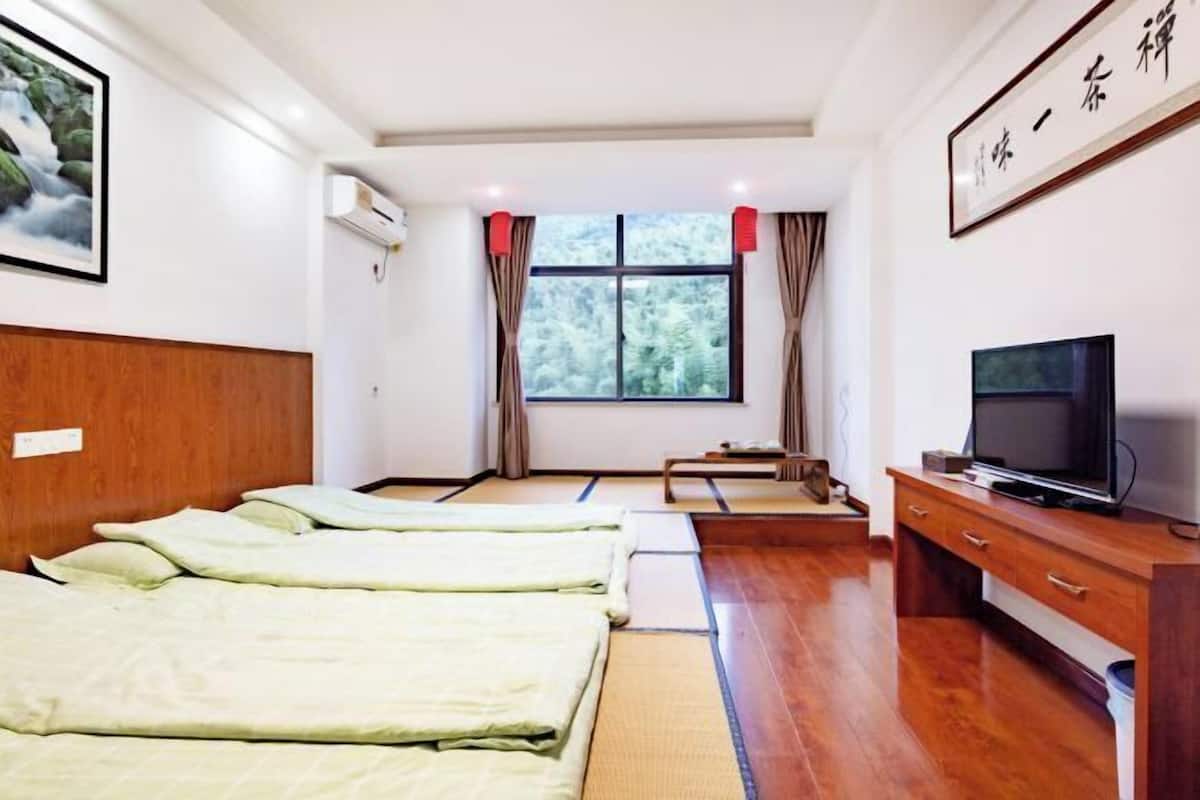 A hotel room with a wooden headboard, a bed with green bedding, a TV on a wooden cabinet, and a window with curtains.