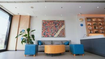 A modern lobby with a sofa, two armchairs, a coffee table, and a large abstract painting.