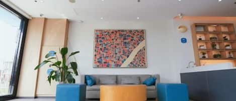 Un hall d’entrée moderne avec un canapé, deux fauteuils, une table basse et un grand tableau abstrait.