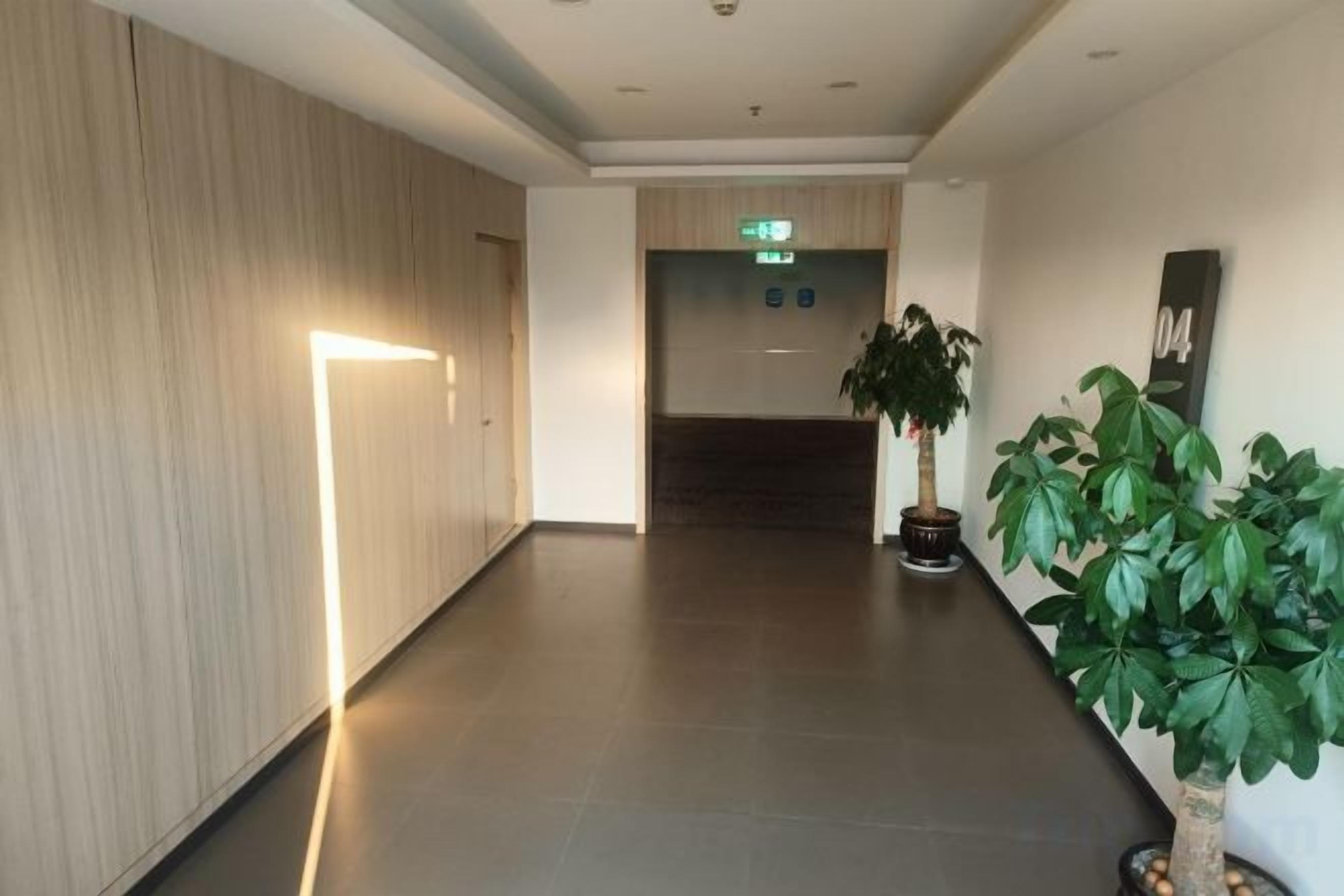 A hallway with a plant, a wall-mounted number sign, and an emergency exit sign.