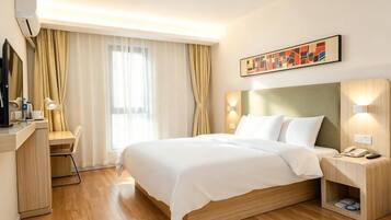 Una habitación de hotel con cama, mesita de noche, escritorio, silla y un gran ventanal con cortinas.