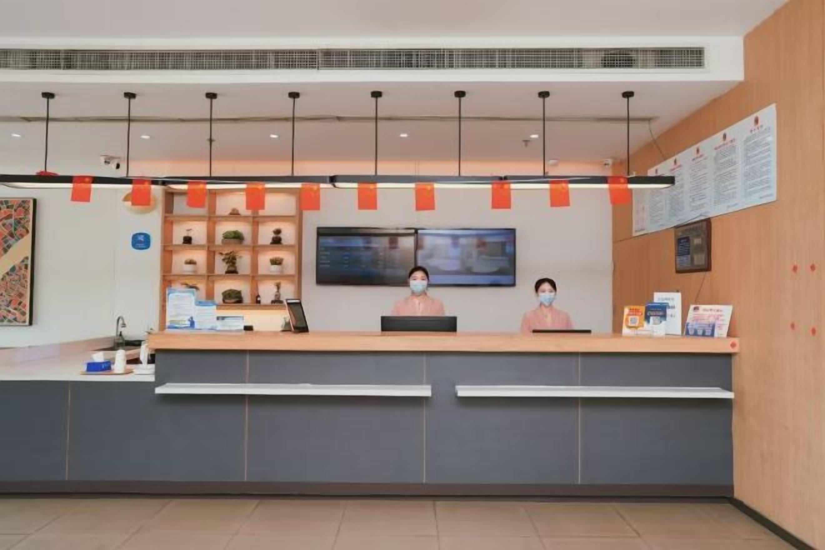 Zona de recepción con mostrador, dos recepcionistas, un televisor y carteles informativos en la pared.