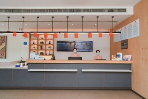 A reception area with a counter, two receptionists, a television, and informational posters on the wall. - Hanting Hotel (Wuxi Qianzhou Wuzhou International Plaza) (Wuxi)