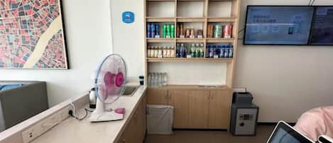 A reception area with a counter, a fan, a shelf with beverages, and a computer monitor.