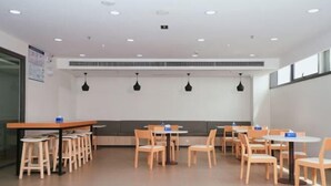 A modern dining area with wooden tables and chairs, recessed ceiling lights, and a bench along the wall. - Hanting Hotel (Wuxi Qianzhou Wuzhou International Plaza) (Wuxi)