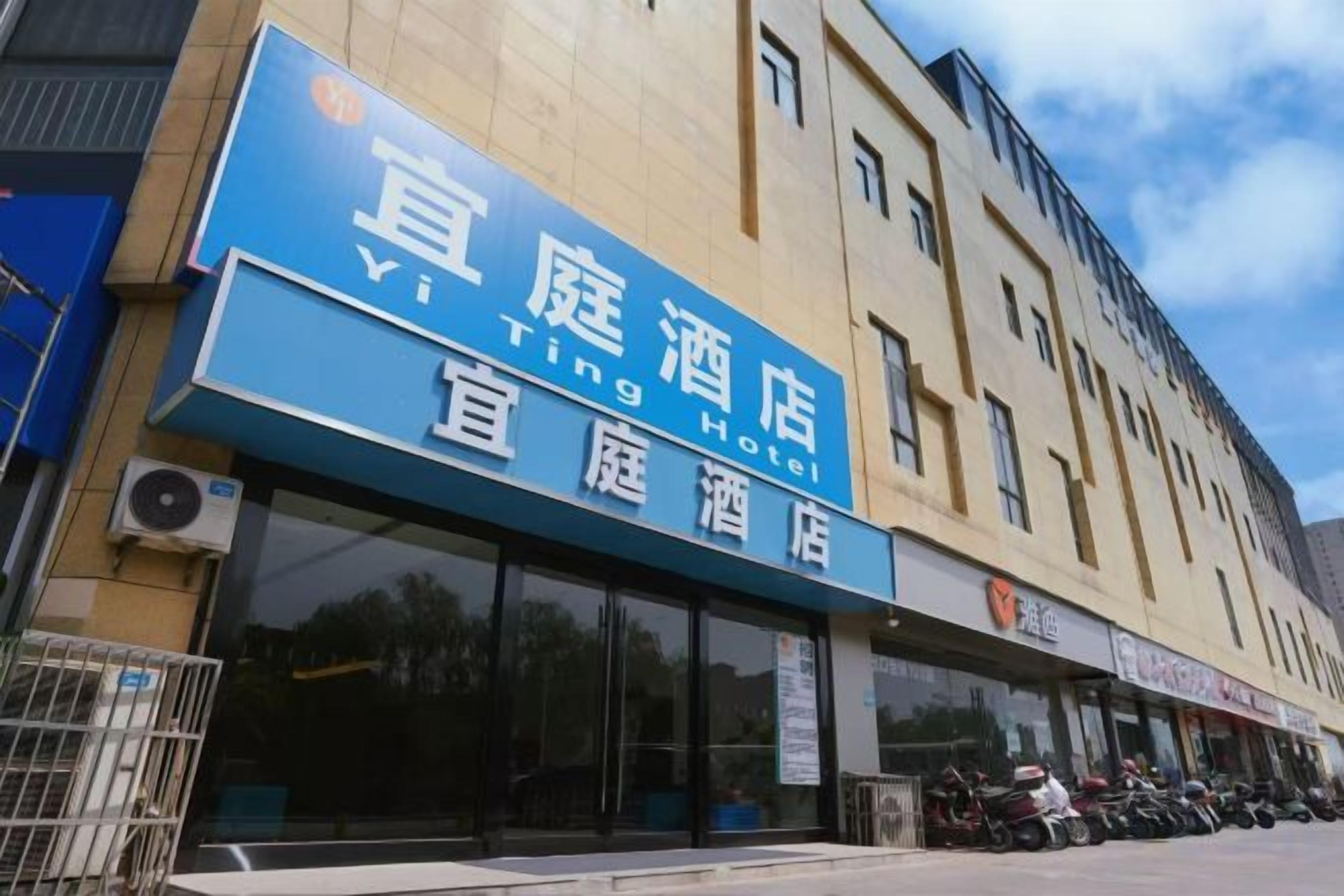 A hotel with a prominent blue sign, large windows, and a row of parked motorcycles outside.