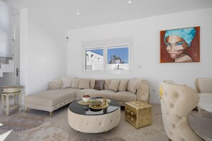 Un salón moderno con un sofá seccional, una mesa de centro redonda, un detalle dorado y un amplio ventanal con vistas.