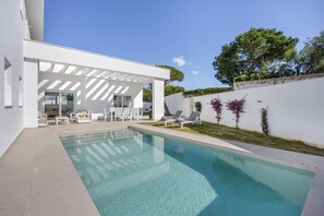 A modern pool area with a clear pool, white lounge chairs, and a covered seating area.