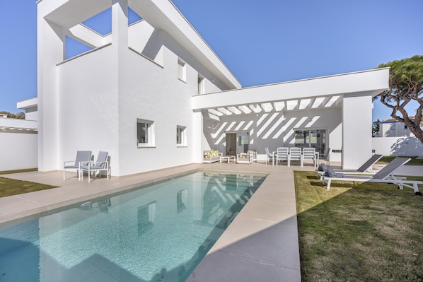 A modern poolside area with a clear pool, white walls, and a pergola structure.