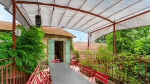 Eine überdachte Terrasse mit Tisch und Stühlen, ein kleines Gebäude mit einer Tür und ein roter Zaun.