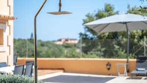 A rooftop terrace with a metal showerhead, outdoor seating, and a large umbrella.