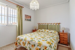 Ein Schlafzimmer mit Bett, Nachttisch, einer Deckenleuchte, einem Fenster mit Vorhängen und einem Bild an der Wand.