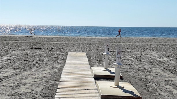 Een houten pad dat naar een strand leidt, met twee witte palen met cijfers.