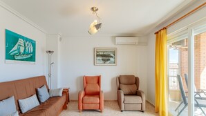 Een woonkamer met een bank, twee fauteuils, een vloerlamp, een plafondlamp, een lijst met een afbeelding en een raam met gordijnen.