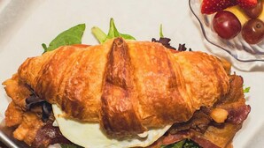Un panino con lattuga, uovo, pancetta e formaggio su un piatto bianco.