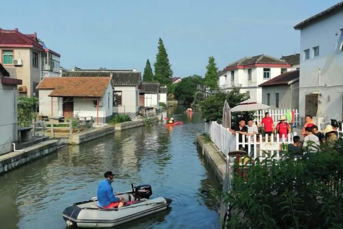 A narrow waterway flanked by traditional buildings, a small boat with a person, and a group of people on the bank.