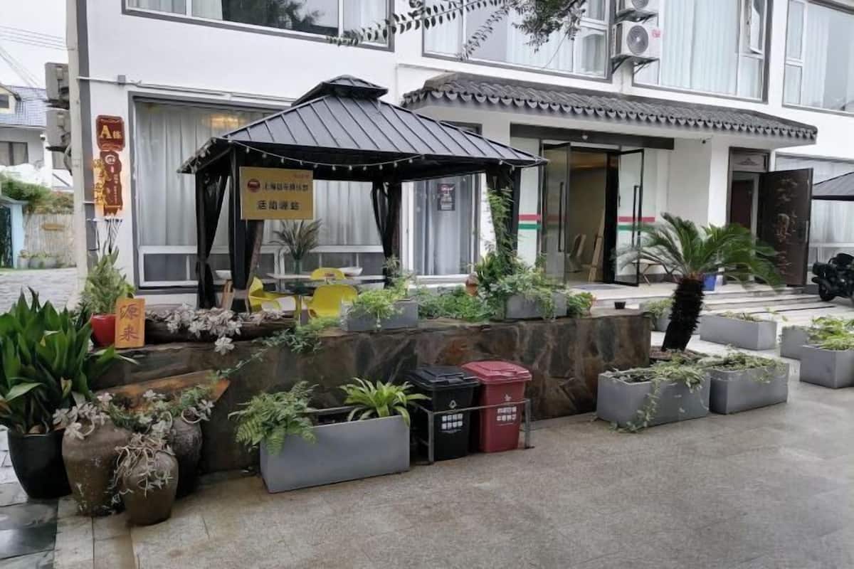 A small outdoor seating area with a metal roof, surrounded by potted plants and a stone wall.
