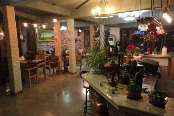Een restaurantinterieur met bakstenen muren, houten tafels, hangende lampen en potplanten.