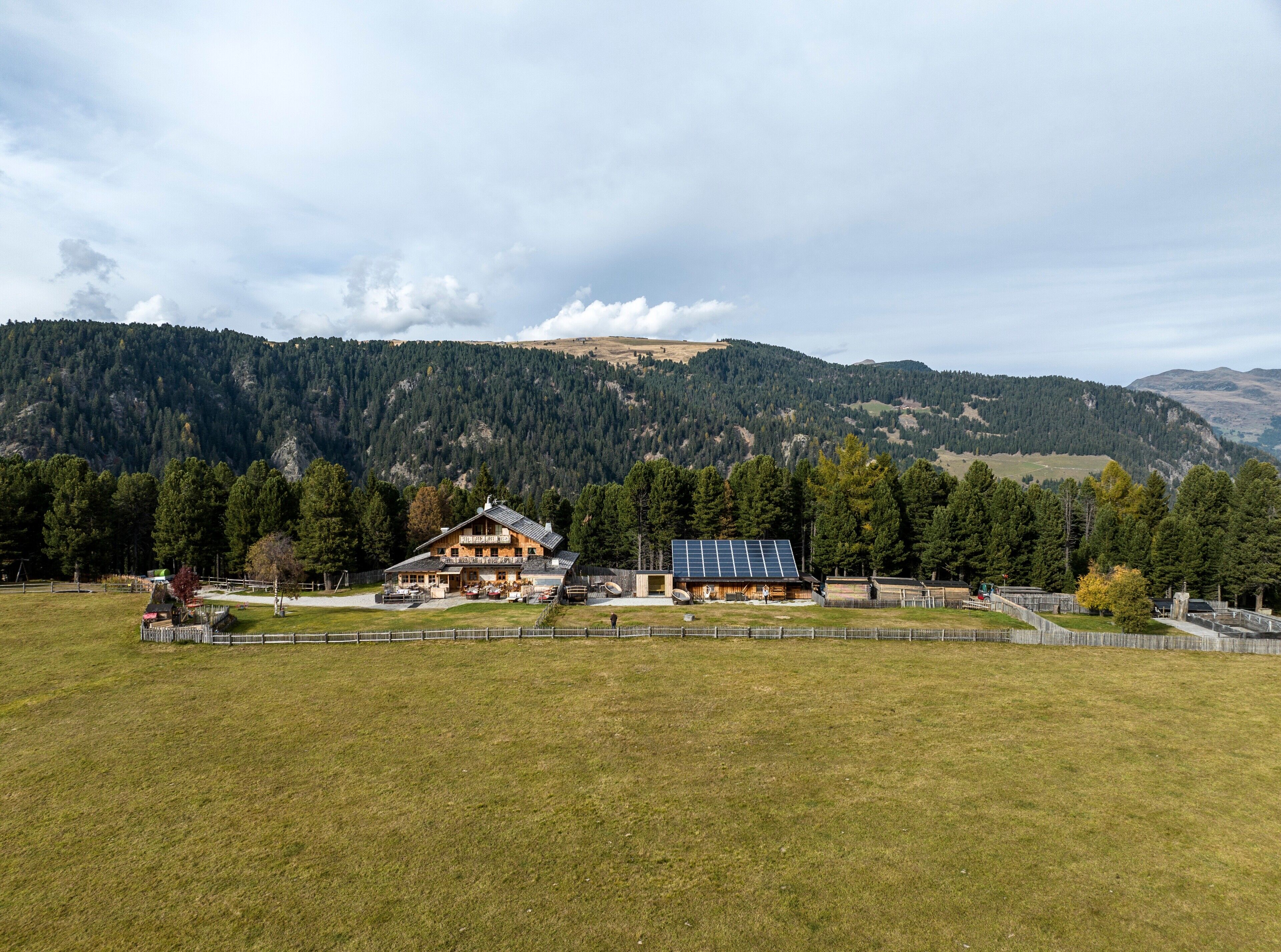 Ein Logis mit einem großen Hauptgebäude und einem Anbau, umgeben von einem eingezäunten Grundstück mit Blick auf die Berge.