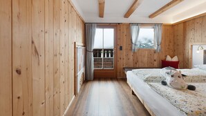 A wooden-paneled room with a bed, a window with curtains, and a view of the outdoors. - Room 'Rot' with Shared Terrace, Shared Garden and Wi-Fi (Villandro)