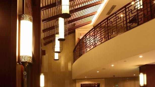 Vestíbulo de hotel de diseño moderno, con una escalera curva, apliques de pared ornamentados y una barandilla con motivos en el nivel superior.