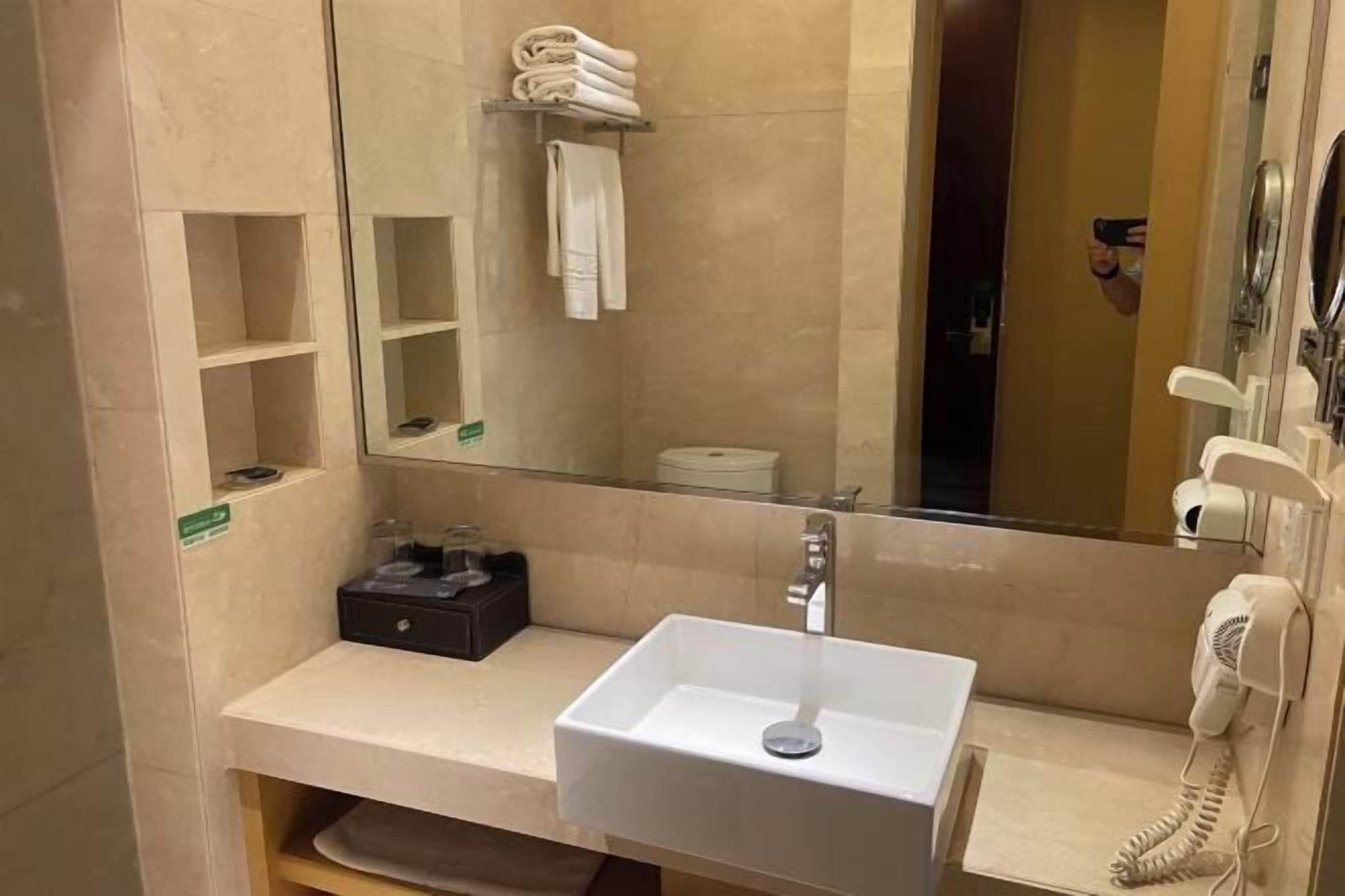 Un baño moderno con un lavamanos blanco, un espejo, un perchero para toallas y un teléfono.