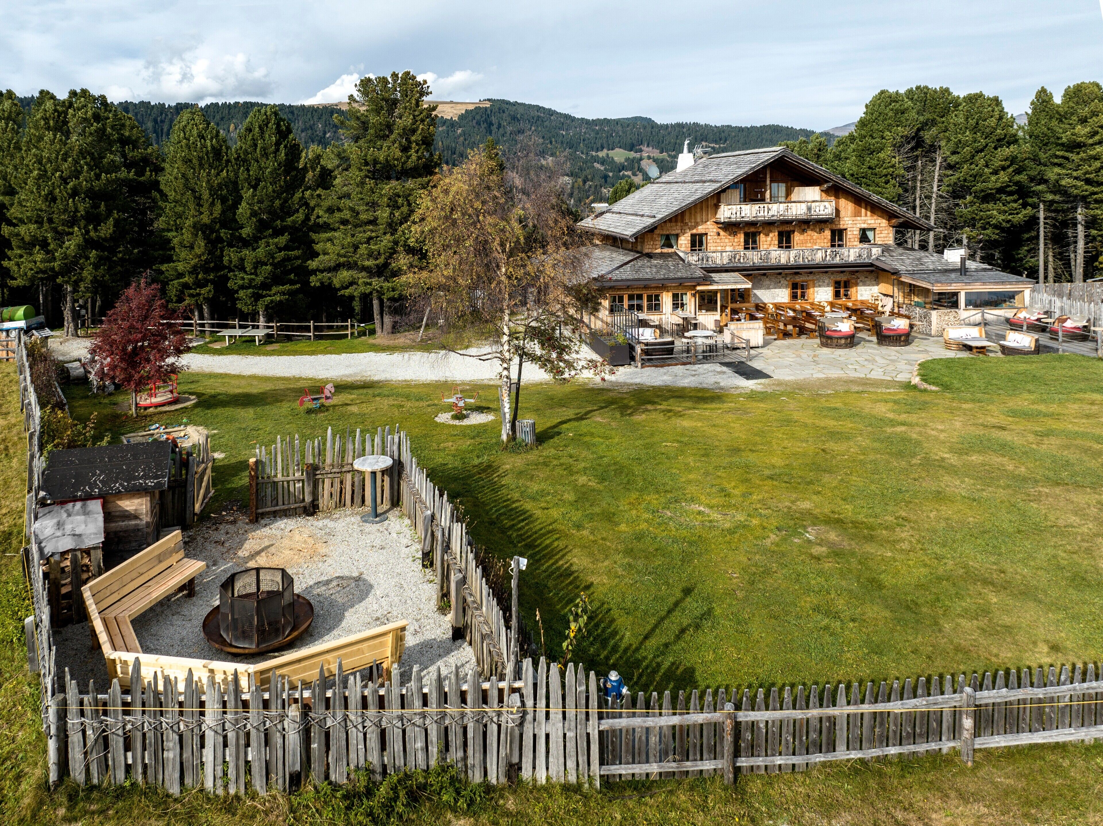 Una cabaña de madera con un patio, asientos al aire libre y vistas del bosque circundante.