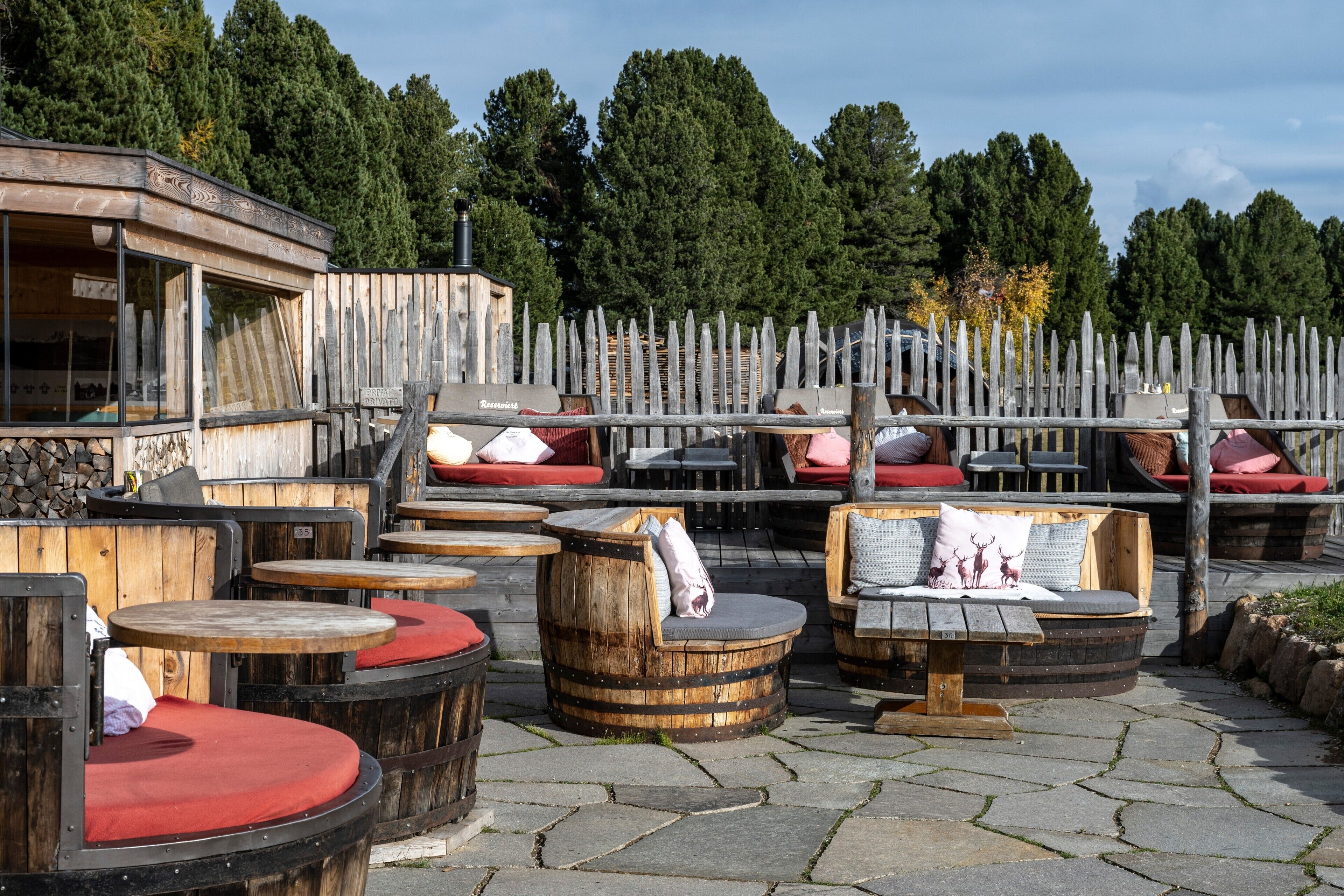Des bancs en bois installés à l’extérieur, agrémentés de coussins rouges, une clôture en bois et un bâtiment avec une enseigne.