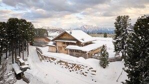 A wooden chalet with a snow-covered roof, surrounded by trees and a stone wall. - Room 'Orange' with Shared Terrace, Shared Garden and Wi-Fi (Villandro)
