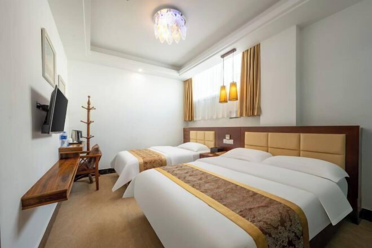 Een hotelkamer met twee bedden, een televisie, een houten bureau, een kapstok en een kroonluchter.