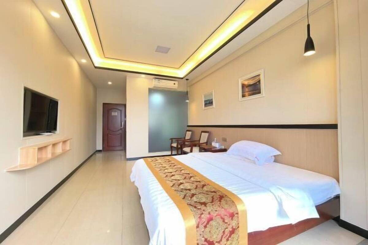 Een hotelkamer met een bed, nachtkastje, lamp en een aan de muur bevestigde televisie.