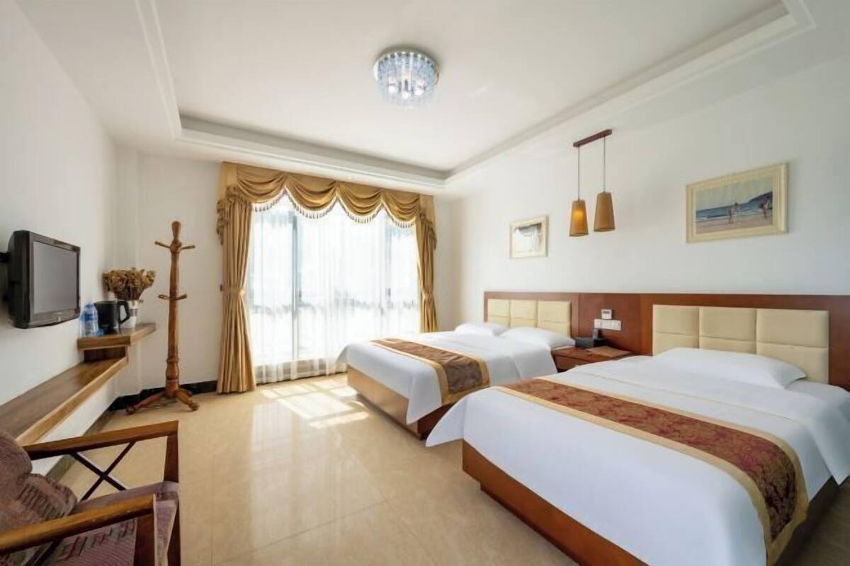 Een hotelkamer met twee bedden, een televisie, een bureau en een raam met gordijnen.
