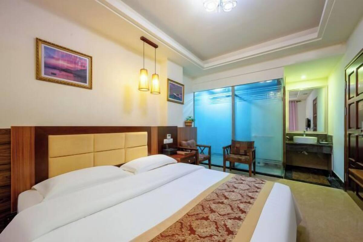 Hotelkamer met een groot bed, een bureau, een stoel, een spiegel en een badkamer zichtbaar door een glazen deur.