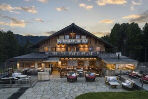 Un edificio in legno di grandi dimensioni con un balcone, posti a sedere all'aperto e un patio in pietra.