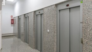 Une rangée d’ascenseurs aux parois en granit, avec un extincteur fixé au mur.