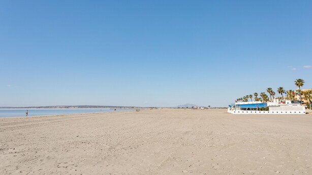 Une plage avec un grand bateau, des palmiers et un ciel dégagé.